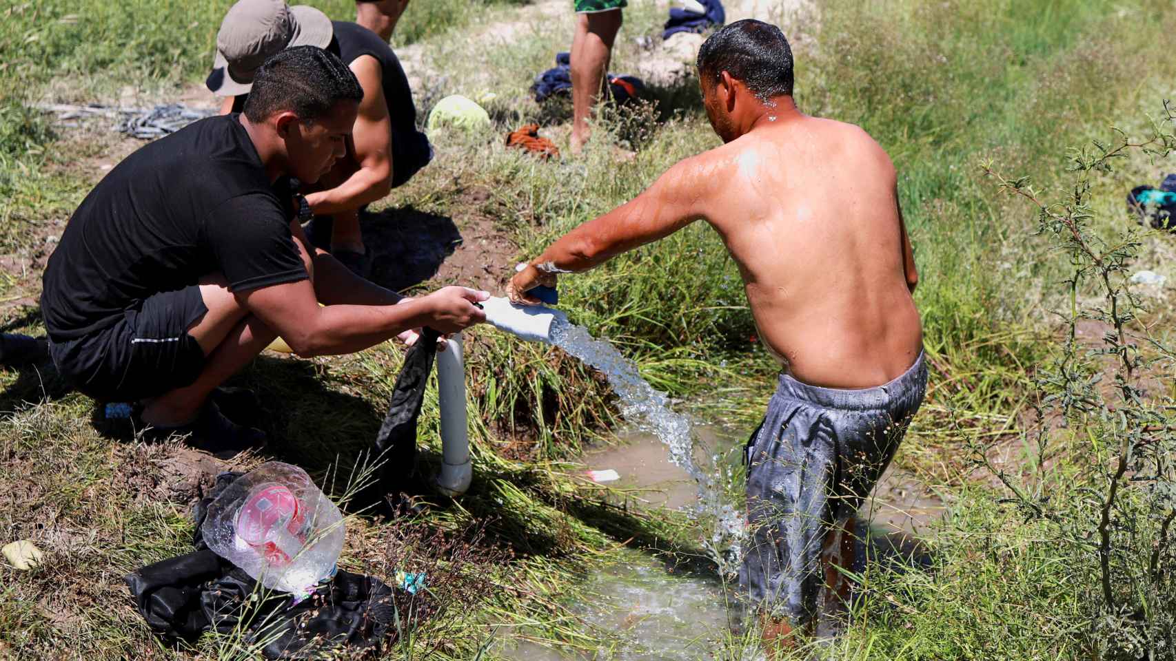 Migrantes se lavan en una acequia cerca de la frontera con EEUU