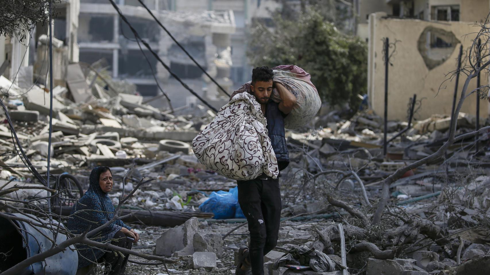 Una mujer sentada entre los escombros del barrio de Al-Ramal observa a un joven transportar dos sacos.