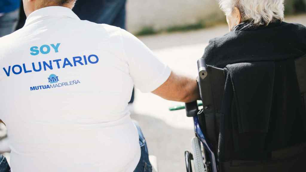 Un voluntario de Mutua Madrileña ayuda a una persona mayor con movilidad reducida en imagen de archivo.